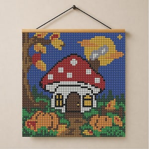 May include: A square diamond painting wall hanging featuring a mushroom-shaped house with a red and white spotted cap. The scene includes a brown tree, a yellow moon in a blue night sky, and green foliage. The artwork is mounted on a wooden frame.