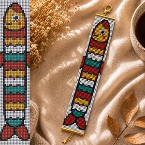 May include: A beaded bracelet featuring a repeating fish pattern in red, yellow, white, and teal colors. The bracelet is constructed with small square beads and finished with gold-toned metal end bars, a lobster claw clasp, and a small star charm.