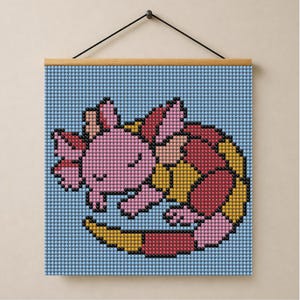 May include: A square diamond painting wall hanging featuring a pixelated, sleeping pink axolotl curled into a circle. The axolotl has light pink skin, darker pink gills, and a body patterned with red and yellow segments against a light blue background.