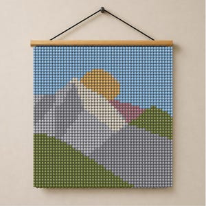 Puede incluir: Un tapiz cuadrado compuesto por pequeñas cuentas esféricas dispuestas en un patrón de paisaje pixelado. El diseño presenta un cielo azul claro, un sol amarillo, montañas grises y colinas verdes, suspendido de una varilla de madera.
