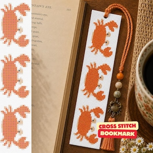 May include: A white fabric bookmark featuring three orange cross-stitched crab designs. The bookmark includes an orange braided cord with three round beads and a small metal crab charm attached to a matching orange tassel at the top end.