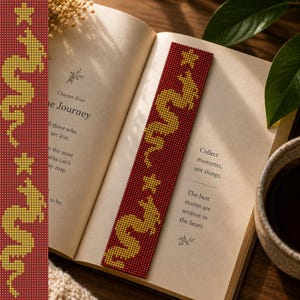 May include: A rectangular bookmark featuring a deep red background with a repeating pattern of yellow pixelated dragons and small yellow stars. The design is composed of a grid of small squares, creating a distinct geometric and digital aesthetic.