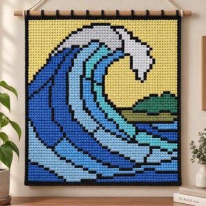 May include: A square crochet wall hanging featuring a pixelated wave design in shades of blue, light blue, and white against a yellow background, with a small green landmass, all framed by a black border and suspended from a wooden rod.