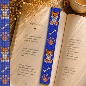 May include: A blue beaded bookmark with a repeating pattern of a cartoon dog, a bone, and a paw print. The bookmark is in an open book with the title "A Quiet Place".