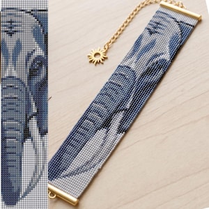 May include: A rectangular beaded bracelet featuring a blue and white elephant head pattern. The bracelet is finished with gold-toned metal end bars and includes a gold-toned chain extender with a small sun-shaped charm at the end of the chain.