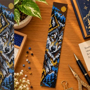 May include: A rectangular beaded bookmark featuring a pixelated wolf head design in shades of gray, white, and black, accented with blue mountain peaks and a yellow moon against a dark brown background, crafted from small uniform seed beads.