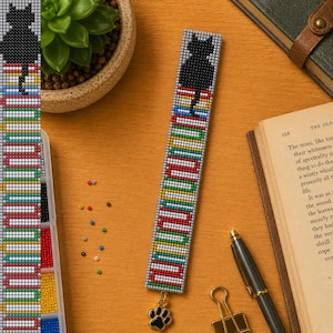 Puede incluir: Un marcapáginas rectangular de cuentas con la silueta de un gato negro sentado sobre una pila de libros coloridos. El diseño utiliza cuentas pequeñas y uniformes en rojo, amarillo, verde, azul y blanco. Un pequeño dije de metal con forma de huella cuelga.
