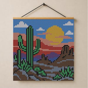 May include: A square diamond painting wall hanging featuring a desert landscape with a tall green saguaro cactus, a large yellow sun, and a multi-colored sky with white clouds. The artwork is mounted on a wooden frame with a black hanging cord.