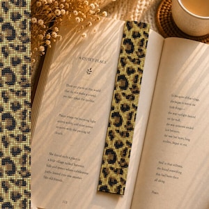 May include: A beaded bookmark with a leopard print pattern is placed in an open book. The bookmark is tan and black. The book is open to a page with the title "A Quiet Place". A second bookmark is visible on the left.