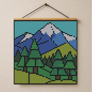 Könnte beinhalten: Ein quadratischer Wandbehang mit einer gepixelten Berglandschaft aus kleinen Perlen. Das Design zeigt schneebedeckte blaue Berge hinter einem Wald aus grünen Tannen und einem hellgrünen Vordergrund, aufgehängt an einer Holzleiste mit schwarzer Kordel.