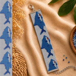 May include: A rectangular beaded bracelet featuring a repeating pattern of blue sharks on a white background. The bracelet is finished with silver-toned metal end bars, a lobster claw clasp, and an adjustable silver-toned chain link extension.