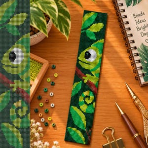 May include: A rectangular beaded bookmark featuring a green chameleon with a large white eye, perched on a dark red branch amidst green leaves. The design is created with small, uniform beads in shades of green, yellow, white, and red.