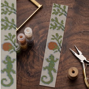 May include: A long, rectangular beaded strip featuring a repeating pattern of green lizards, orange circles, and light green leafy branches on a white background, accompanied by small clear jars of beads and metal jewelry pliers.