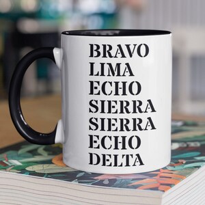 May include: White ceramic mug with a black handle and black rim. The mug has the words "BRAVO LIMA ECHO SIERRA SIERRA ECHO DELTA" printed in black on the front.