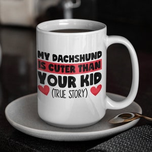 May include: White coffee mug with black text that reads "My Dachshund is cuter than your kid (true story)" with two red hearts.