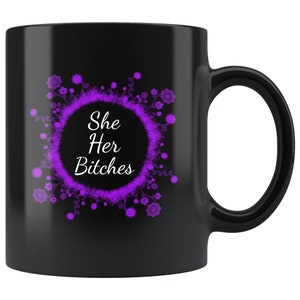 May include: Black ceramic mug with a purple floral design surrounding the text "She Her Bitches". The mug has a black handle and a glossy finish. The text is in a white, bold font.