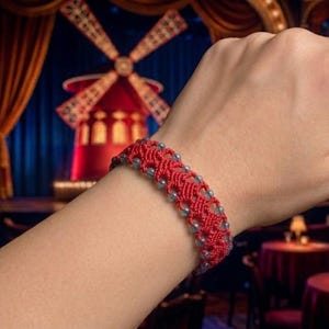 May include: A red macrame bracelet featuring a complex woven cord pattern integrated with small, translucent, light-colored beads arranged in a repeating sequence along the length of the band, creating a textured and detailed accessory.