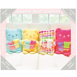 May include: Four plush gummy bear cushions in different colours: blue, yellow, pink, and multi-coloured. Each bear has a pocket with smaller gummy bears inside. The image includes the text "Gummy Bear Cushion", "Stitch by hand", "Sewing by machine", "Tutorial", "With Mini bear", "PDF Pattern", and "Easy steps!"