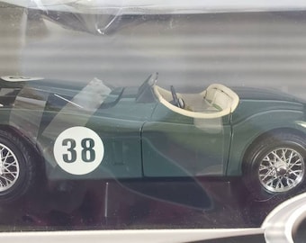 Op de afbeelding: Een 1:18 schaalmodel van een vintage Jaguar XK120 roadster in groen met een wit interieur. Het model heeft een wit race nummer "38" aan de zijkant en wordt getoond in een transparante kunststof vitrine.