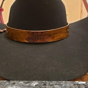 May include: A black cowboy hat with a wide brim and a brown leather band with a floral design.