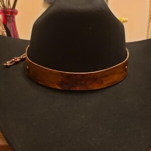 May include: A black cowboy hat with a wide brim and a brown leather band around the crown.