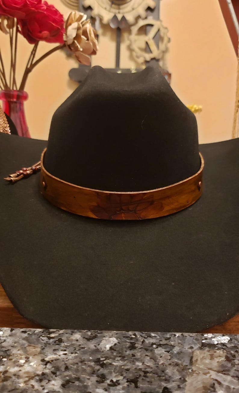 May include: A black cowboy hat with a wide brim and a brown leather band around the crown.