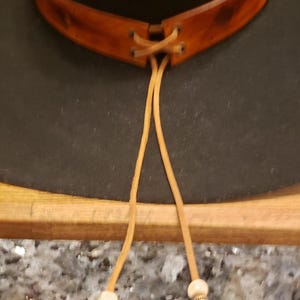 May include: A black felt cowboy hat with a brown leather band and beaded tie. The hat has a wide brim and a tall crown.