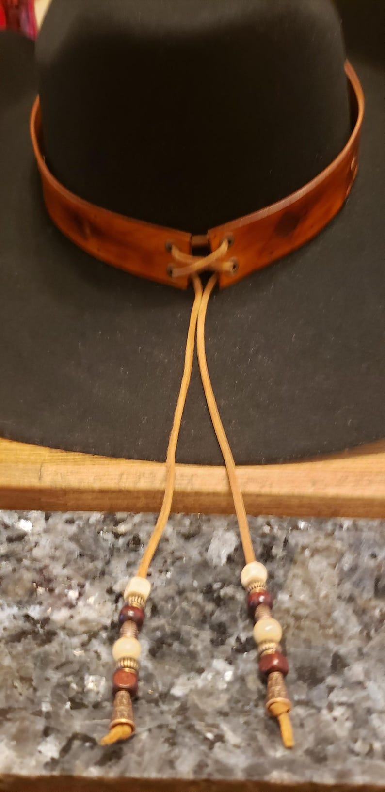 May include: A black felt cowboy hat with a brown leather band and beaded tie. The hat has a wide brim and a tall crown.