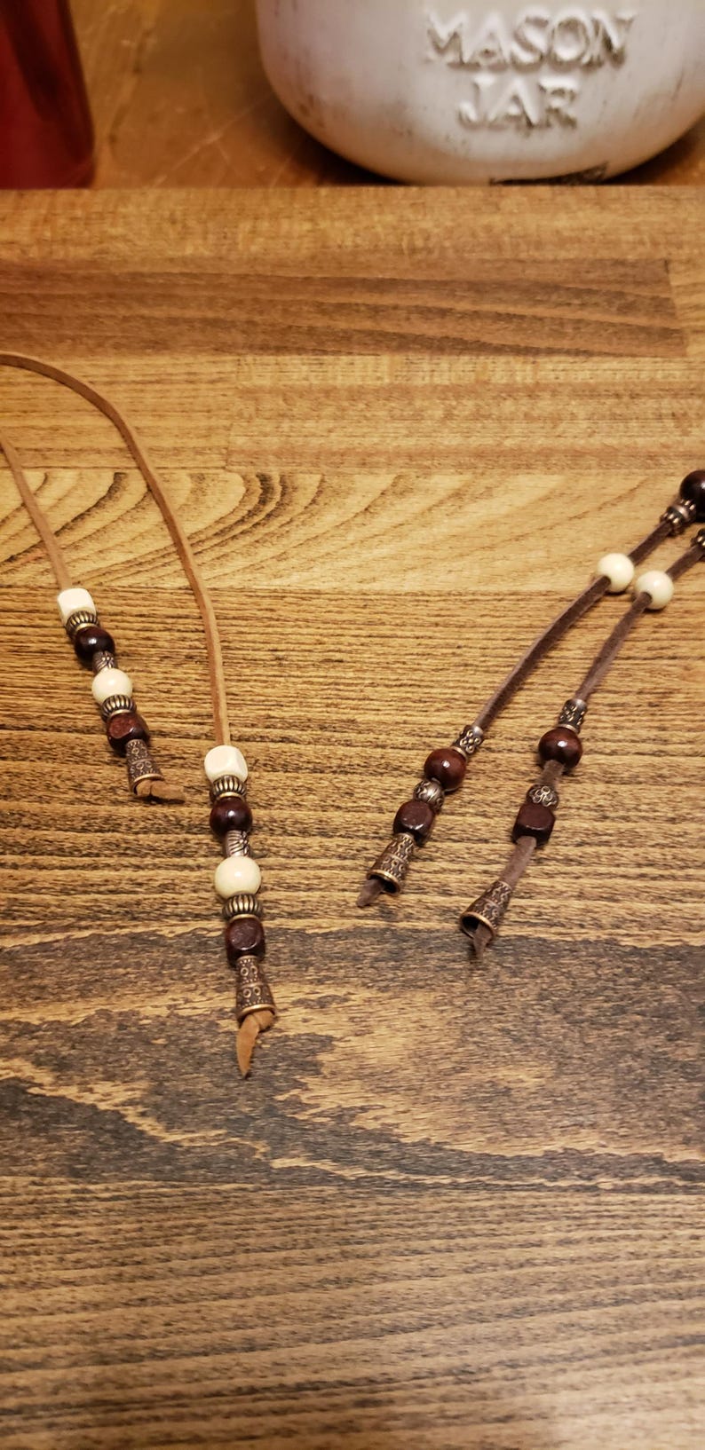 May include: Two brown leather cords with brown and white beads and metal accents. The cords are tied at the ends.