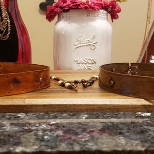 May include: Two brown leather belts with decorative floral designs. The belts are on a wooden surface.