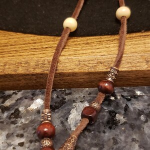 May include: A brown leather cord with wooden beads and metal accents. The cord is tied in a knot at the end.