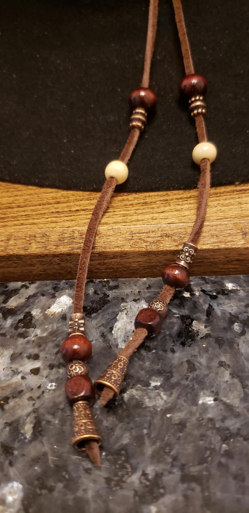 May include: A brown leather cord with wooden beads and metal accents. The cord is tied in a knot at the end.