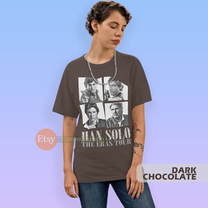 May include: A dark brown t-shirt with a graphic of four images of Han Solo from different Star Wars movies. The text "Han Solo The Eras Tour" is printed below the images.