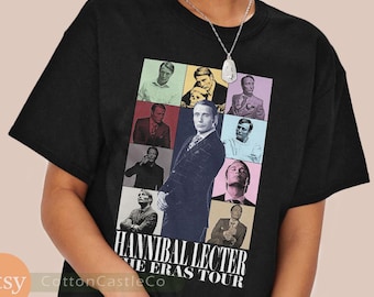 Pode incluir: Camiseta preta com um design gráfico que apresenta várias imagens de Hannibal Lecter. O design inclui o texto "Hannibal Lecter The Eras Tour". A camiseta é feita de um material macio.