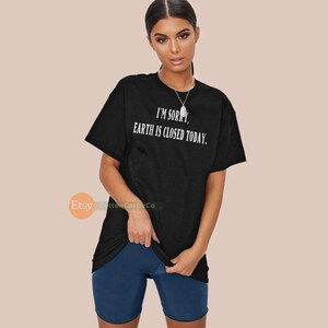 May include: Black t-shirt with the text "I'M SORRY, EARTH IS CLOSED TODAY." The shirt is a classic crew neck style. The model is also wearing dark blue shorts.