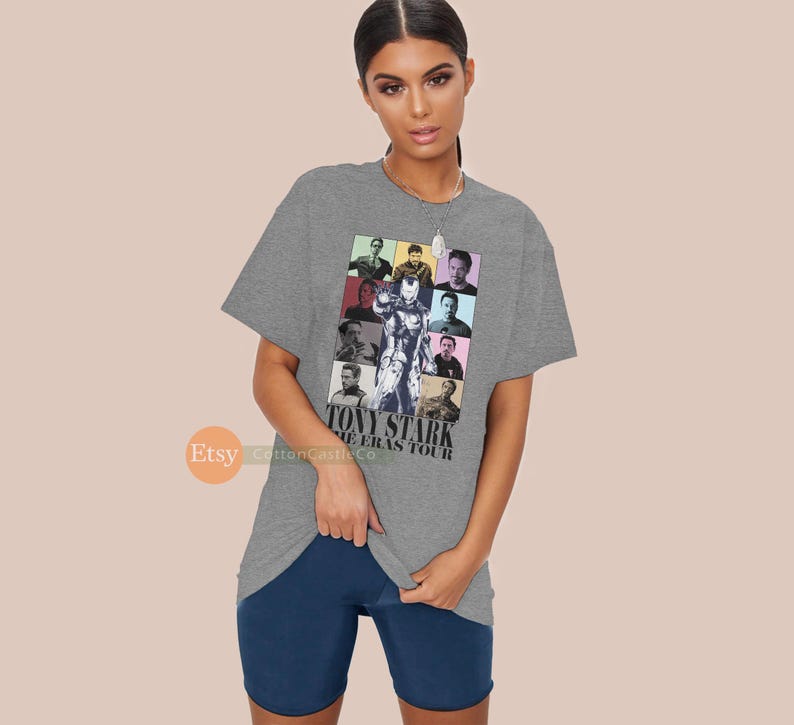 May include: Grey t-shirt featuring a collage of images of Tony Stark from the Iron Man films. The text "Tony Stark The Eras Tour" is printed on the shirt.