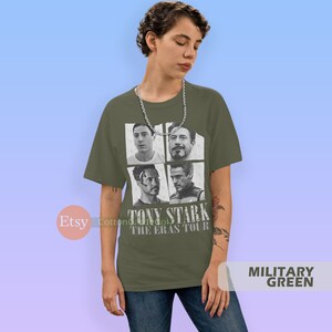 以下が含まれることがあります： アイアンマン映画のトニー・スタークの白黒写真4枚をコラージュした緑色のTシャツ。Tシャツには「TONY STARK THE ERAS TOUR」の文字がプリントされています。