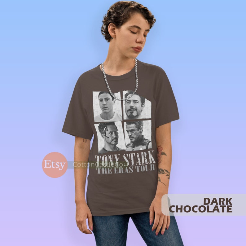 以下が含まれることがあります： アイアンマンの映画からトニー・スタークの白黒画像がプリントされたダークブラウンのTシャツ。画像はトニー・スタークの4つの異なるバージョンを示しており、画像の下には「トニー・スターク・ザ・エラス・ツアー」というテキストが書かれている。