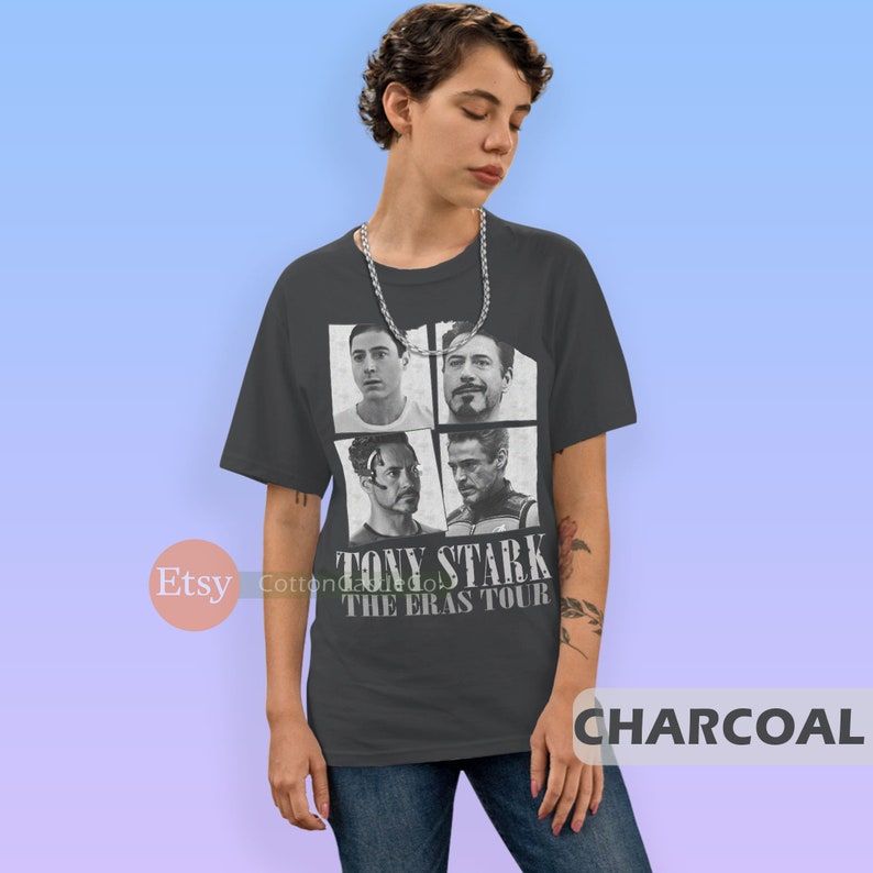 以下が含まれることがあります： アイアンマン映画のトニー・スタークの白黒写真4枚をコラージュした、チャコールグレーのTシャツ。Tシャツには「TONY STARK THE ERAS TOUR」の文字が白でプリントされています。