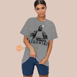 Peut inclure: T-shirt gris avec une image en noir et blanc d'un homme assis sur une chaise avec le texte "LEBOWSKI" en dessous.