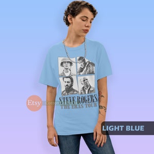 May include: Light blue t-shirt with a black and white image of Steve Rogers from the Marvel Cinematic Universe. The image shows four different versions of Steve Rogers, including his appearance in Captain America: The First Avenger, Captain America: The Winter Soldier, Captain America: Civil War, and Avengers: Endgame. The text "Steve Rogers The Eras Tour" is printed below the image.