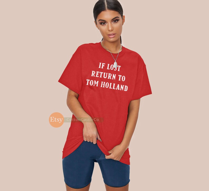 May include: Red t-shirt with white text that reads "IF LOST RETURN TO TOM HOLLAND".