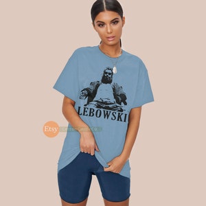 Peut inclure: Un t-shirt bleu clair avec une image en noir et blanc d'un homme barbu assis sur une chaise. Le texte "LEBOWSKI" est imprim&eacute; sous l'image.