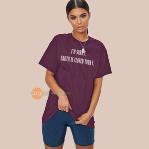 May include: A maroon t-shirt with the text "I'M SORRY, EARTH IS CLOSED TODAY." in white. The shirt is paired with navy blue shorts. The image is of a person wearing the shirt and shorts.