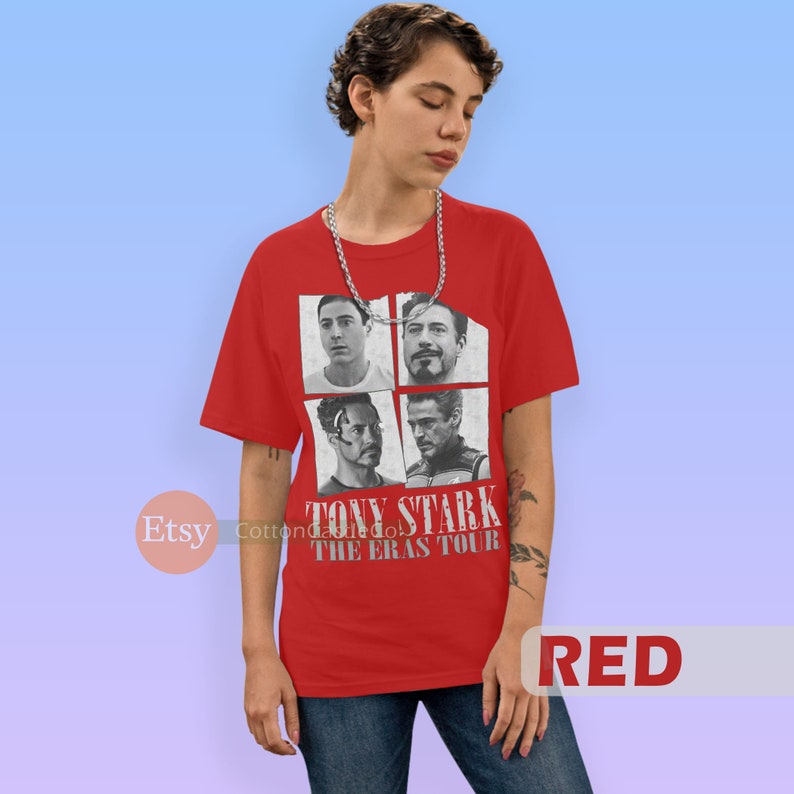 以下が含まれることがあります： アイアンマン映画のトニー・スタークの異なる4つの画像のグラフィックがプリントされた赤いTシャツ。Tシャツには「トニー・スターク・ザ・エラス・ツアー」の文字がプリントされています。