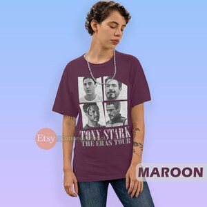 以下が含まれることがあります： アイアンマン映画のトニー・スタークの画像4枚がプリントされた、マルーンのTシャツ。Tシャツには「トニー・スターク・ザ・エラス・ツアー」の文字がプリントされています。