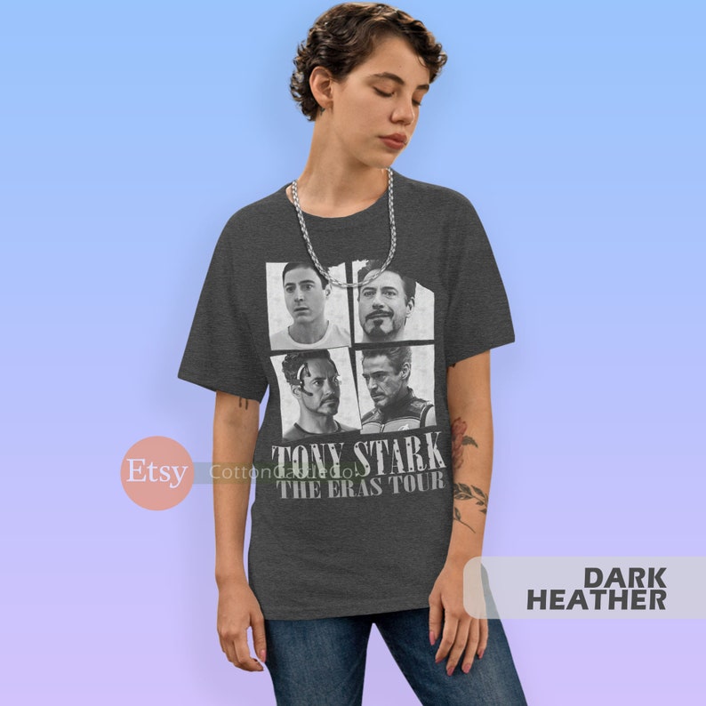 以下が含まれることがあります： ダークヘザーグレーのTシャツに、アイアンマン映画のトニー・スタークの画像4枚のコラージュがプリントされています。Tシャツには「トニー・スターク・ザ・エラス・ツアー」の文字が白でプリントされています。