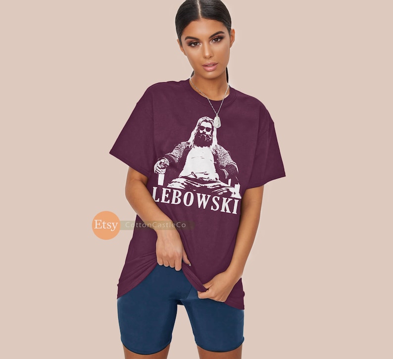 Peut inclure: T-shirt bordeaux avec un graphique blanc d'un homme assis sur un tr&ocirc;ne avec une boisson &agrave; la main. Le texte "The Dude Abides" est imprim&eacute; sous le graphique.