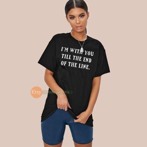 May include: Black t-shirt with the text "I'M WITH YOU TILL THE END OF THE LINE" in white. The shirt is paired with dark blue shorts. The model is wearing a silver necklace.