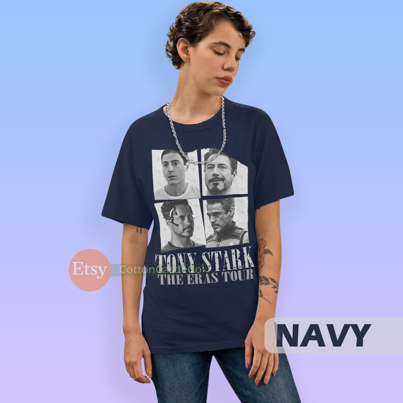 以下が含まれることがあります： アイアンマン映画のトニー・スタークの4つの画像をコラージュしたネイビーブルーのTシャツ。Tシャツには「TONY STARK THE ERAS TOUR」の文字が白でプリントされています。